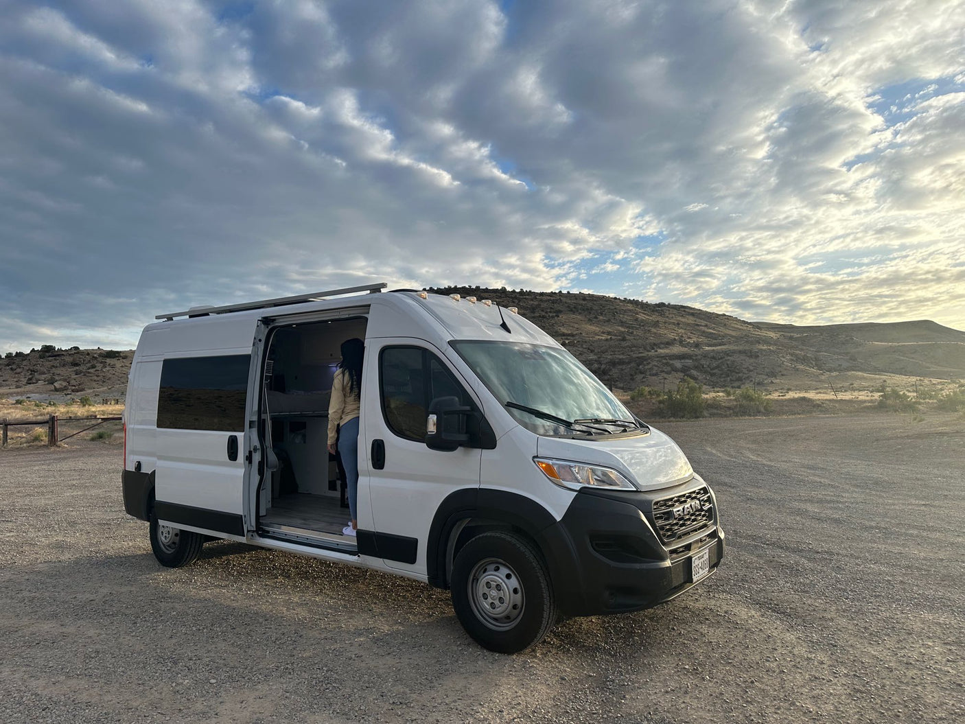 White camper van, door open with person inside, parked in a scenic gravel area. Ideal for an RV rental outdoor adventure.