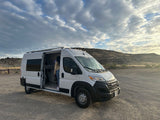White camper van, door open with person inside, parked in a scenic gravel area. Ideal for an RV rental outdoor adventure.