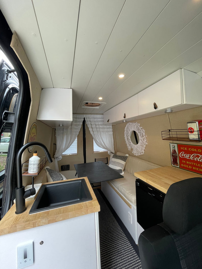 This RV rental showcases a stylish interior with a wood-top kitchen and black sink, a flexible dining table, and built-in lounge seating. — photo 6