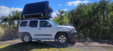 This RV rental alternative, a white Nissan Xterra with a deployed rooftop tent, is ready for your outdoor camping adventure.