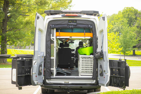 Open back of a white custom camper van revealing an upper bunk, seating, and storage. Perfect setup for an RV rental.