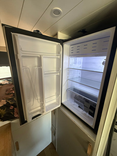 This image shows a clean, empty mini-fridge inside an RV rental, featuring shelves and a crisper drawer, ready for use.