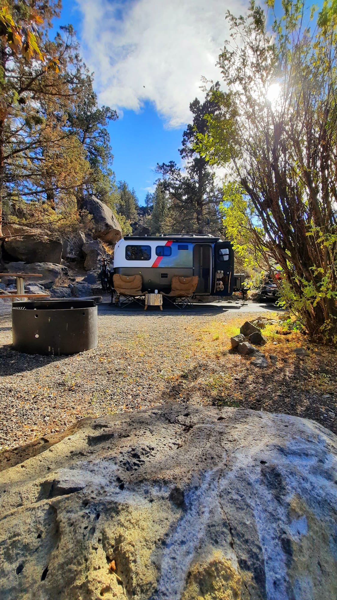 Serene RV rental campsite with a stylish camper trailer, chairs, and fire pit, nestled among trees & rocks. — photo 20