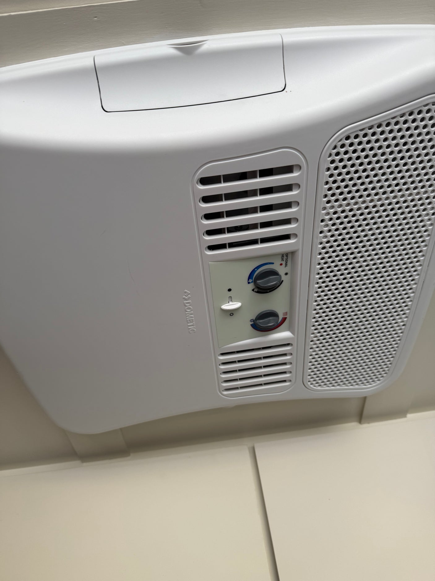 White Dometic RV rental air conditioner on ceiling with control panel, showing fan, temperature, and optional heat.