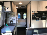 Interior view of an rv rental camper van, featuring a kitchenette, bed, and a detailed control panel with power and water gauges.