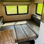 RV rental's adaptable interior: a clean dinette setup that converts to a bed, with windows showing green scenery. — photo 14