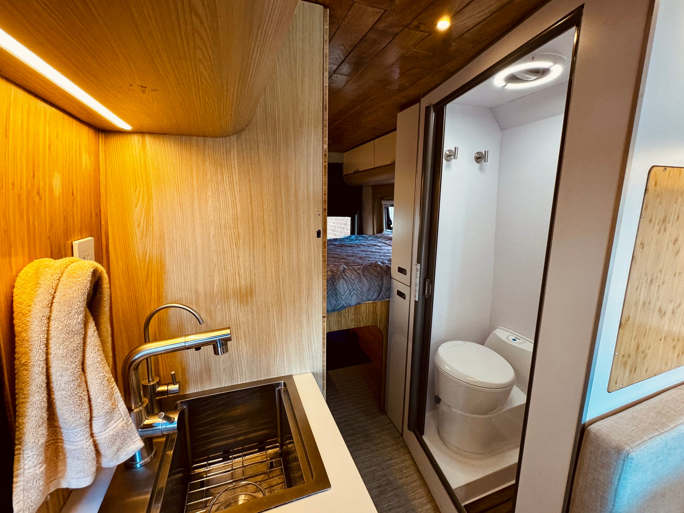 This RV rental boasts a modern wood interior, featuring a compact kitchen with sink, wet bath, and cozy bed for comfortable travel.