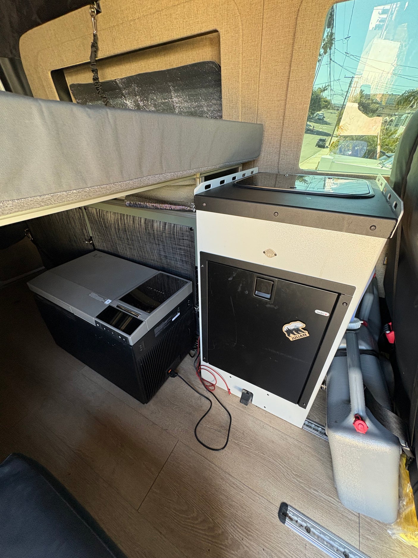 Inside an rv rental: compact camper van kitchen, portable fridge/ice maker, and raised bed setup for mobile living.