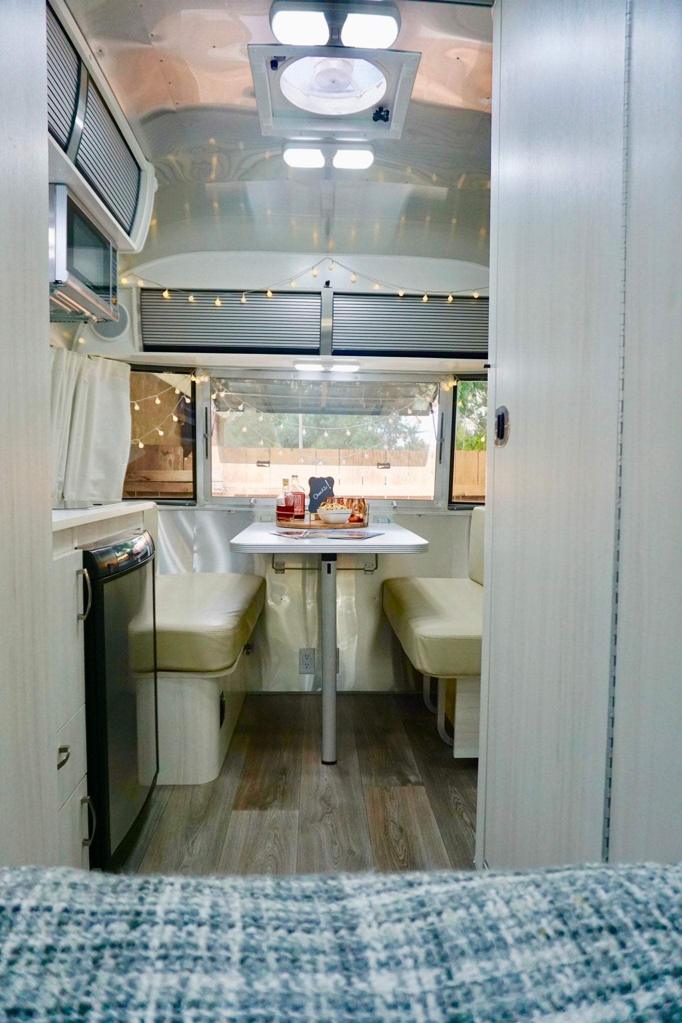 Inside a modern RV rental: a bright dining area with table, cream benches, and kitchen space, illuminated by string lights. — photo 10