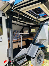 Open Taxa TigerMoth off-grid camper for rv rental. Reveals compact interior with table, seating, and rugged off-road exterior.
