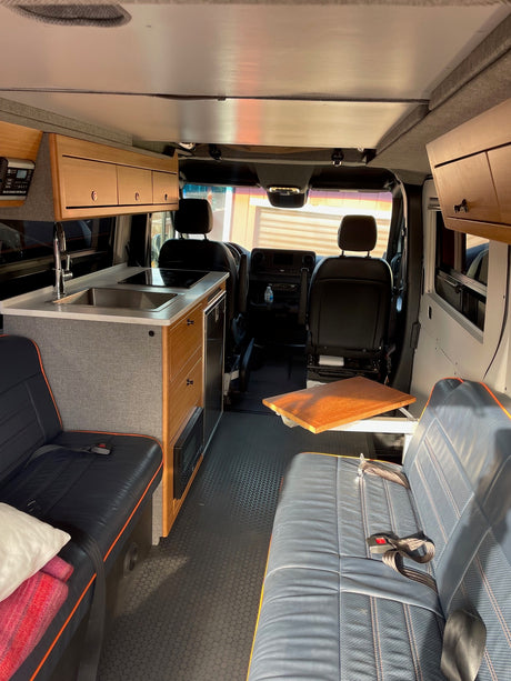 Compact rv rental interior with kitchen, lounge seating, and overhead cabinets for a comfortable mobile lifestyle.