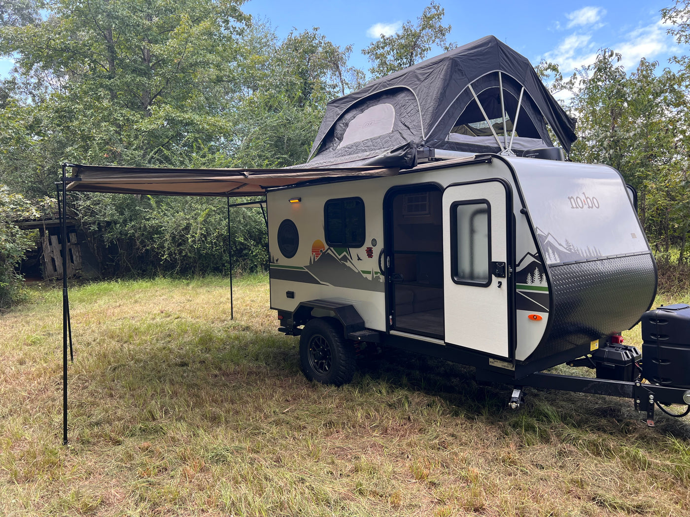 Explore the outdoors with this 'no-bo' travel trailer rv rental, complete with a rooftop tent and extended awning in a grassy spot. — photo 11