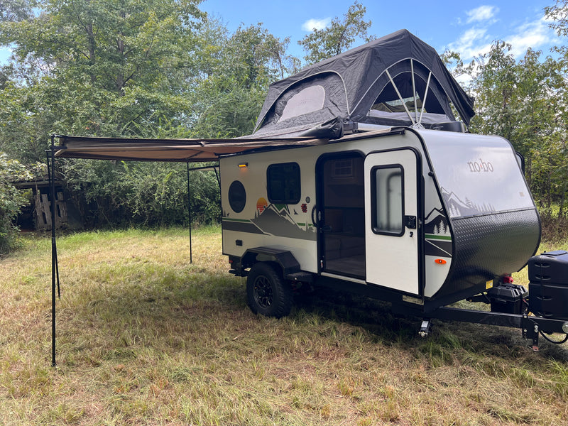 Explore the outdoors with this 'no-bo' travel trailer rv rental, complete with a rooftop tent and extended awning in a grassy spot. — photo 11