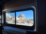 Inside an RV rental: a window view of stunning desert rock formations under a bright blue sky.