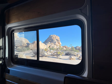 Inside an RV rental: a window view of stunning desert rock formations under a bright blue sky.