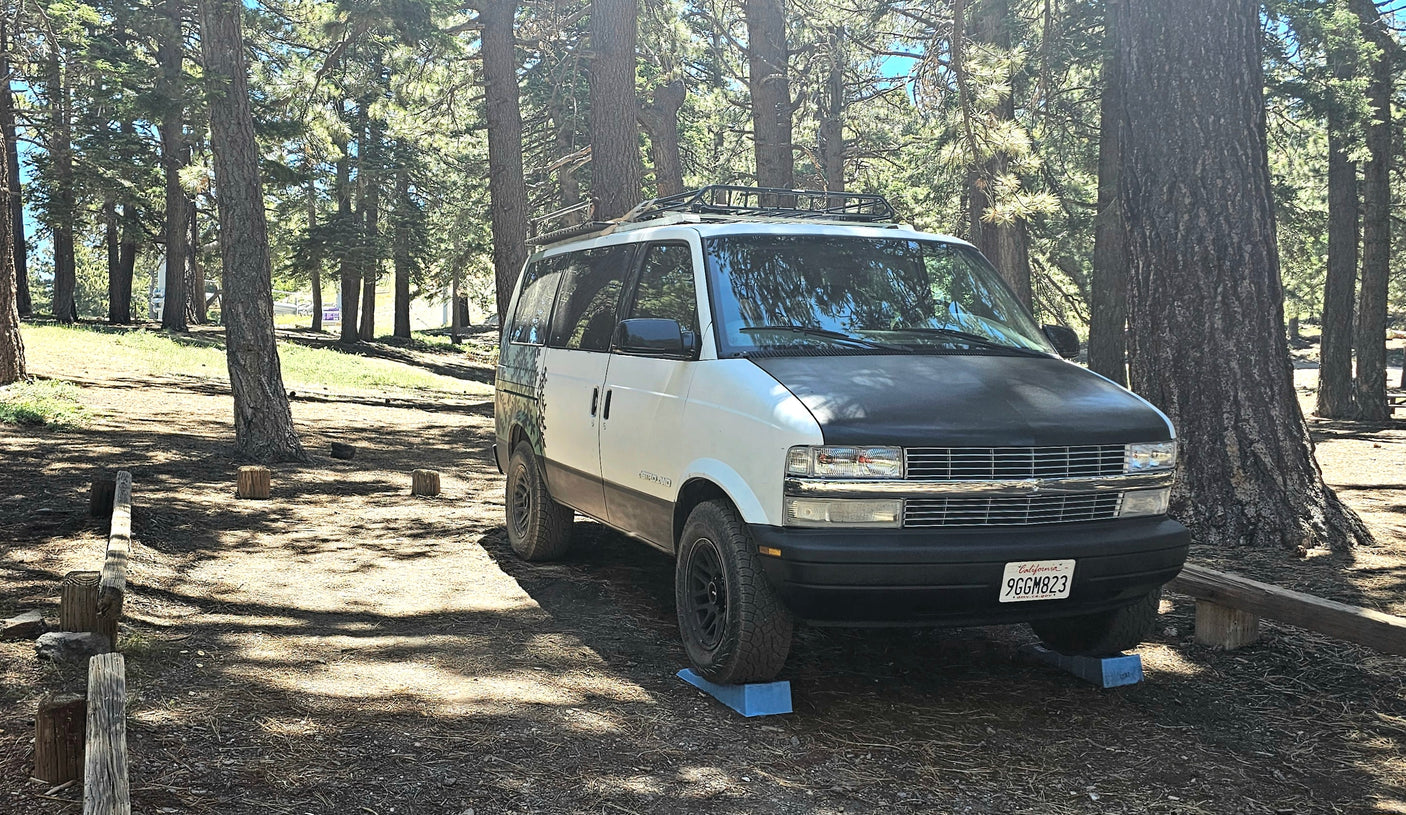 White & black RV rental camper van leveled in a sunny California forest campsite. Ideal for outdoor adventures.