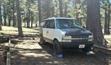White & black RV rental camper van leveled in a sunny California forest campsite. Ideal for outdoor adventures.