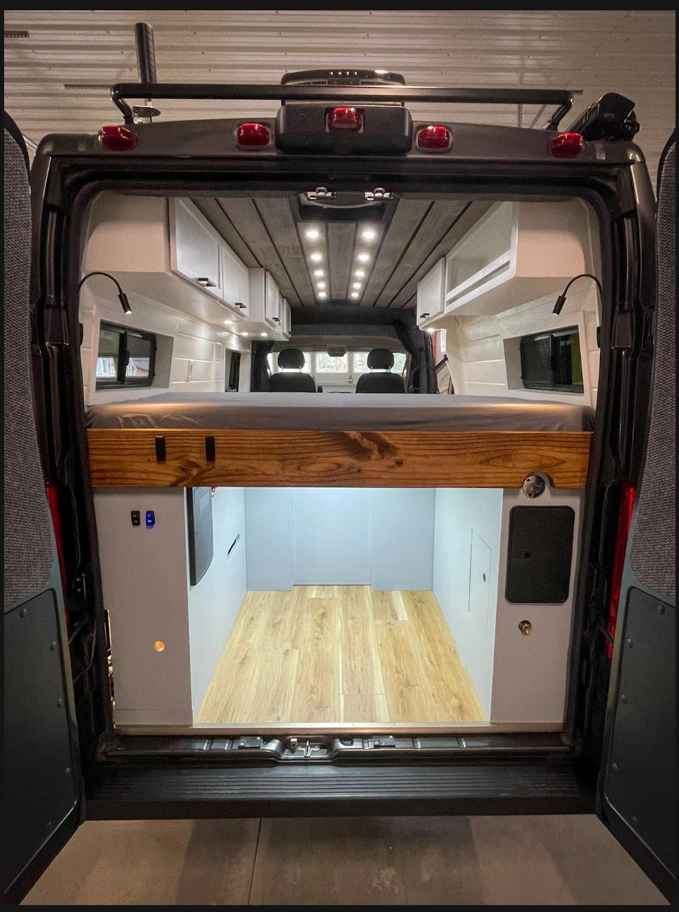 Inside an RV rental, this custom camper van features an elevated bed, overhead cabinets, and large rear storage space.