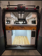 Inside an RV rental, this custom camper van features an elevated bed, overhead cabinets, and large rear storage space.