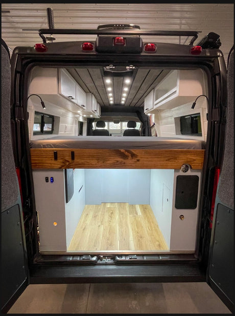 Inside an RV rental, this custom camper van features an elevated bed, overhead cabinets, and large rear storage space.