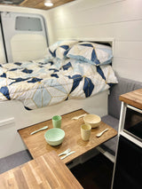 Inside an RV rental: a compact camper van featuring a bed, dining area with modern dishes, and kitchenette.
