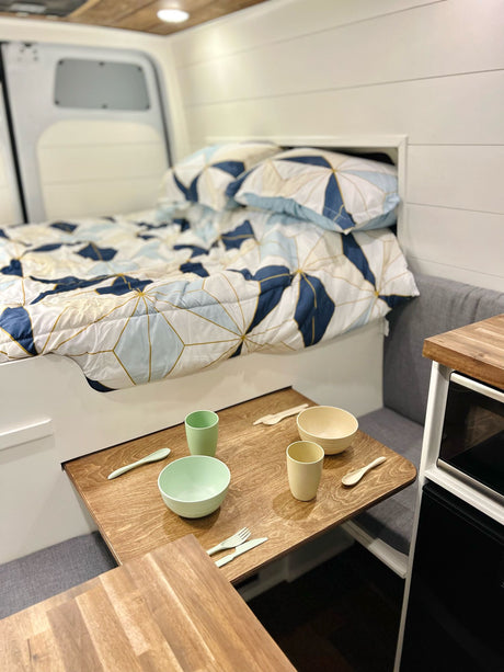 Inside an RV rental: a compact camper van featuring a bed, dining area with modern dishes, and kitchenette.