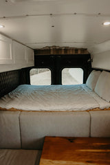 Spacious RV rental bedroom featuring a full bed, large windows, storage cabinets, and cozy seating. Ready for adventure!