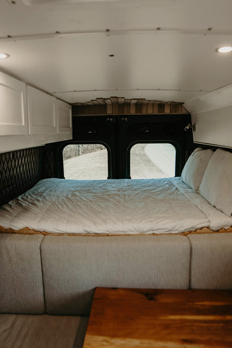 Spacious RV rental bedroom featuring a full bed, large windows, storage cabinets, and cozy seating. Ready for adventure!
