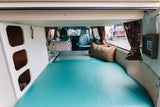 Inside a bright custom RV rental with a wide teal bed, compact kitchen, and inviting front cabin. Ideal for road trips!
