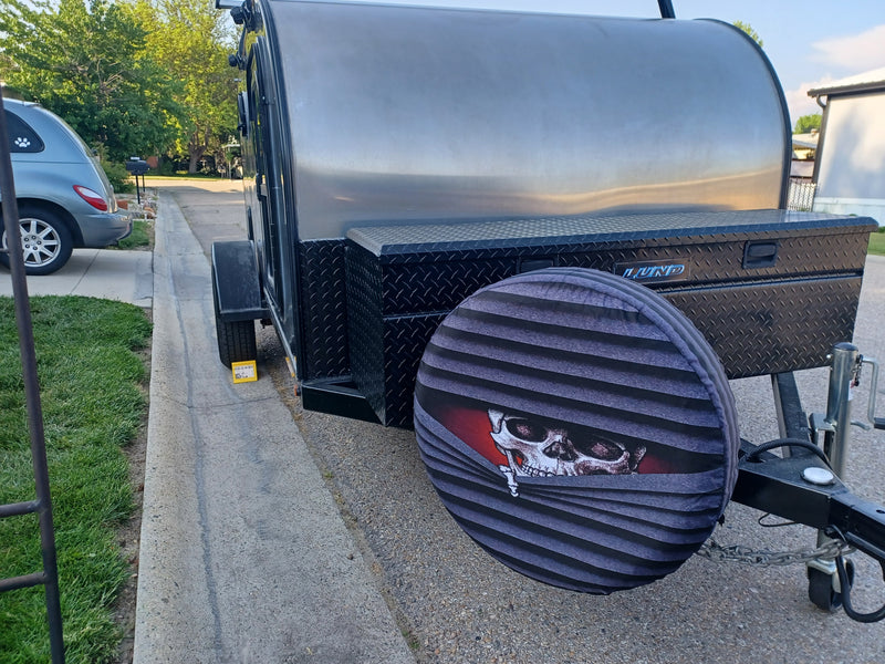 This RV rental is a sleek, silver teardrop trailer with a custom skull spare tire cover and black diamond plate storage. A car is visible. — photo 4