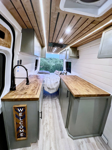 Cozy, modern rv rental interior: kitchen, bed, wood-paneled ceiling, and scenic views from the back. Bright & inviting.