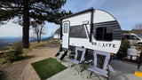 A Go Lite travel trailer rv rental is set up with chairs at a scenic mountain campsite, offering panoramic views.