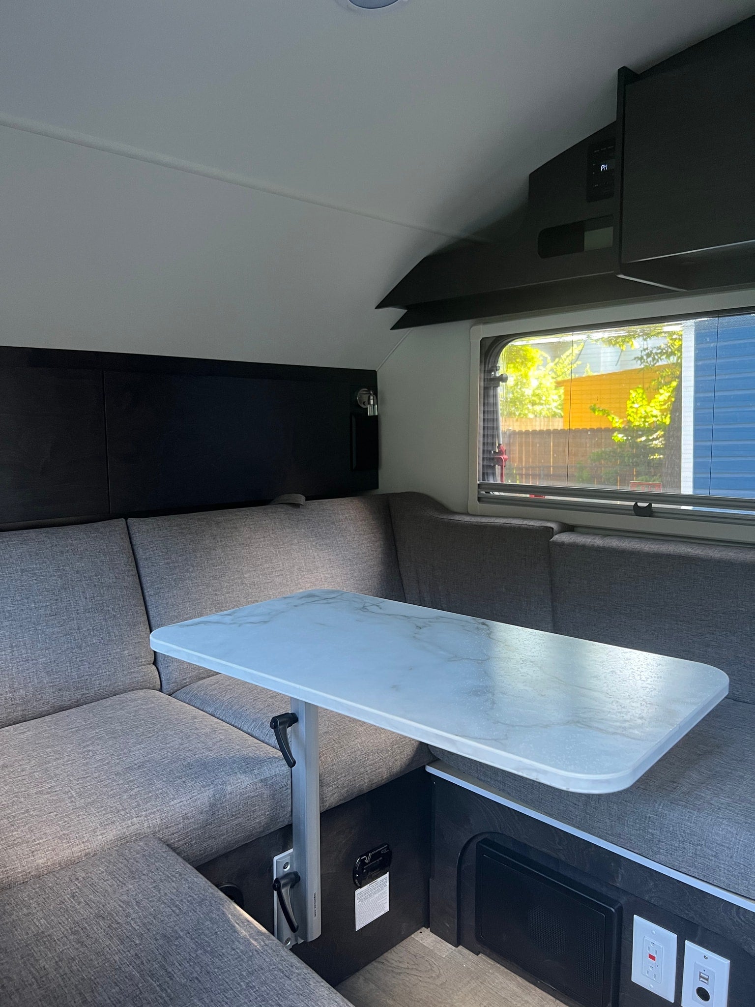 Cozy RV rental interior showing a grey upholstered dinette with a white marble-patterned adjustable table by a window.