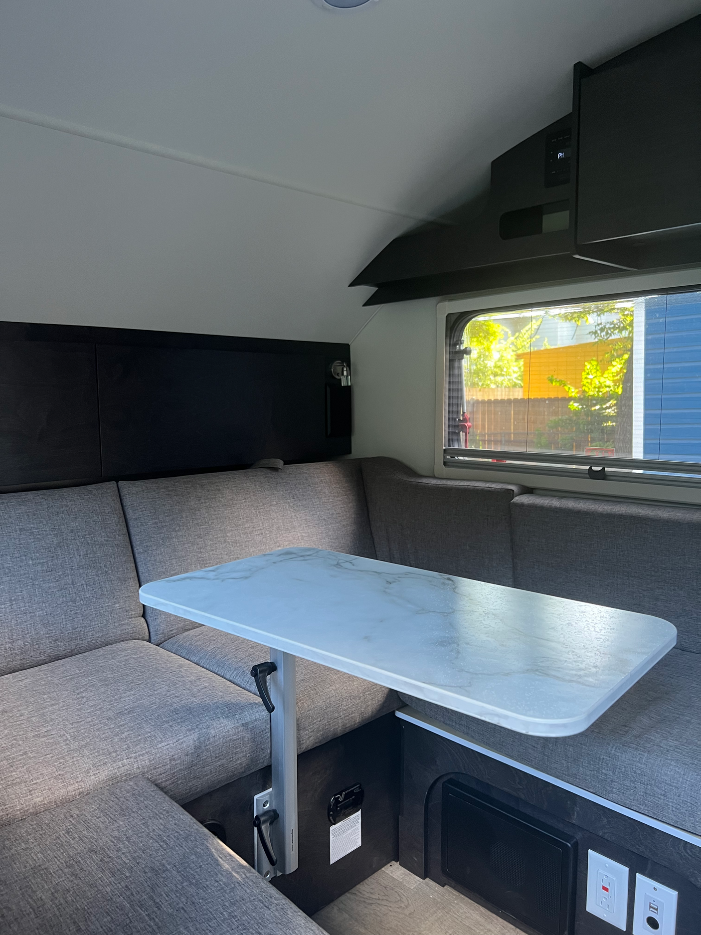 Cozy RV rental interior showing a grey upholstered dinette with a white marble-patterned adjustable table by a window.