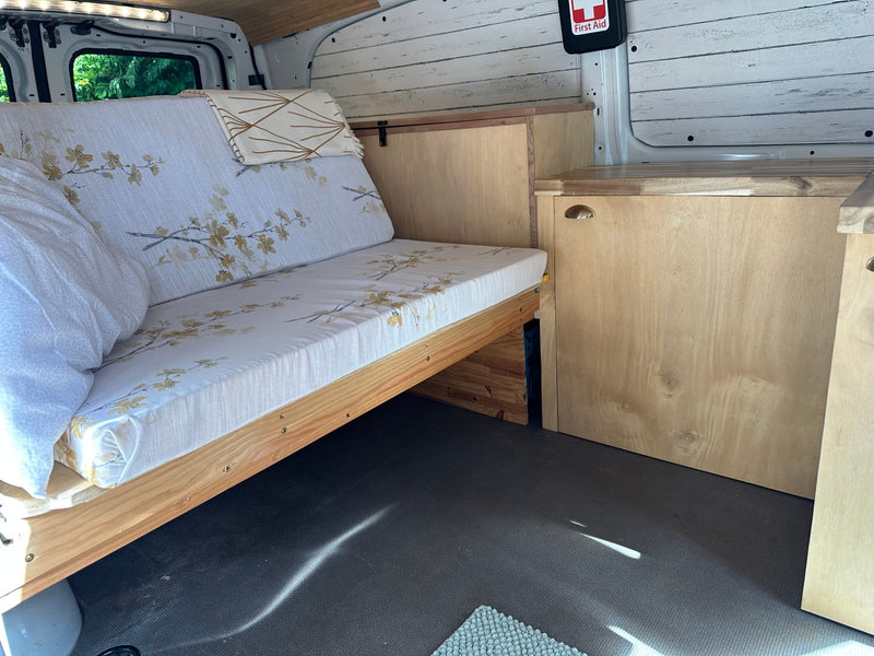 This RV rental's cozy van interior features a floral cushion bed, wooden cabinetry, and white shiplap walls. — photo 10