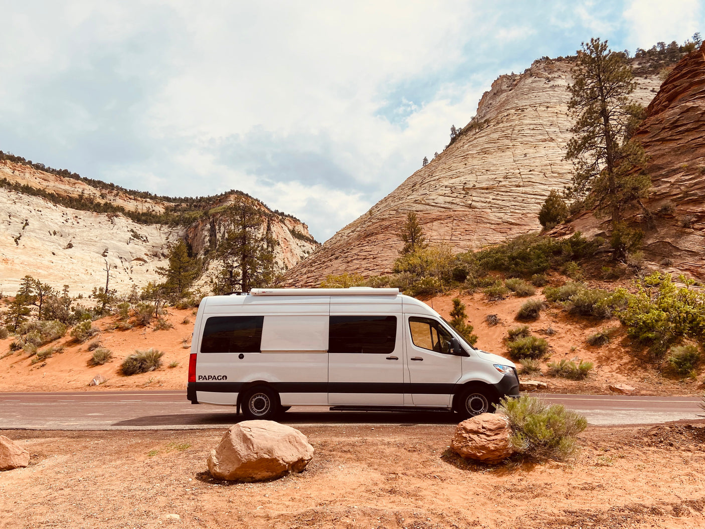 Scenic RV rental: A white Papago camper van parked on a dirt pullout with stunning layered desert mountains.