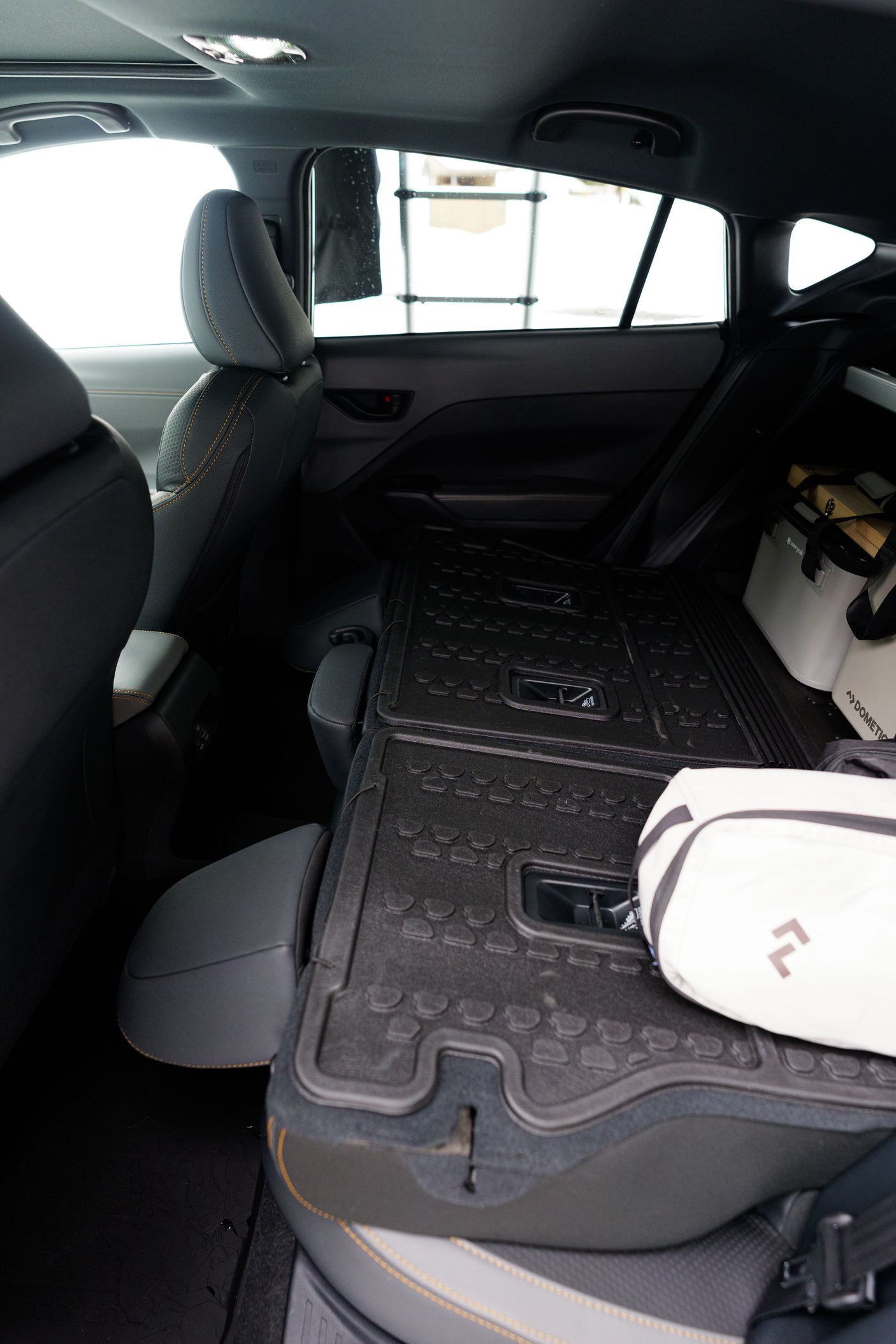 Car interior with folded rear seats & durable cargo mats, ready for an RV rental road trip. Cooler & gear stored securely.