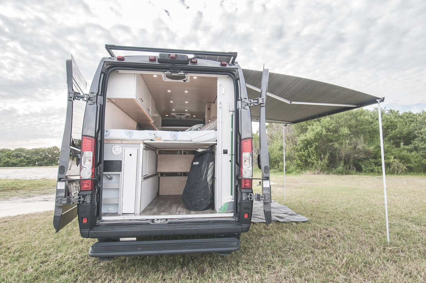 This RV rental shows a camper van's custom interior, bed, and storage, with an extended awning for shaded outdoor living.