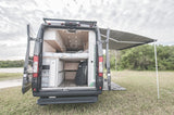 This RV rental shows a camper van's custom interior, bed, and storage, with an extended awning for shaded outdoor living.