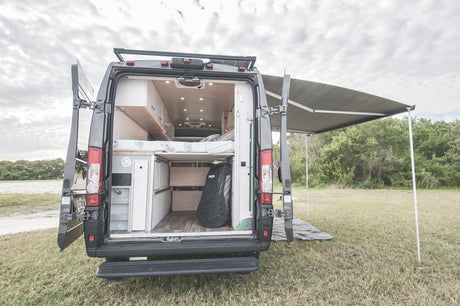 This RV rental shows a camper van's custom interior, bed, and storage, with an extended awning for shaded outdoor living.