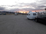 White compact RV rental and SUV parked on a gravel lot. Sunset glows over distant mountains and palm trees.