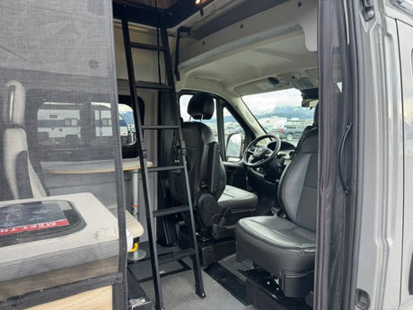 Interior of an RV rental, showcasing the driver's cockpit, passenger seat, and a ladder leading from the living space.