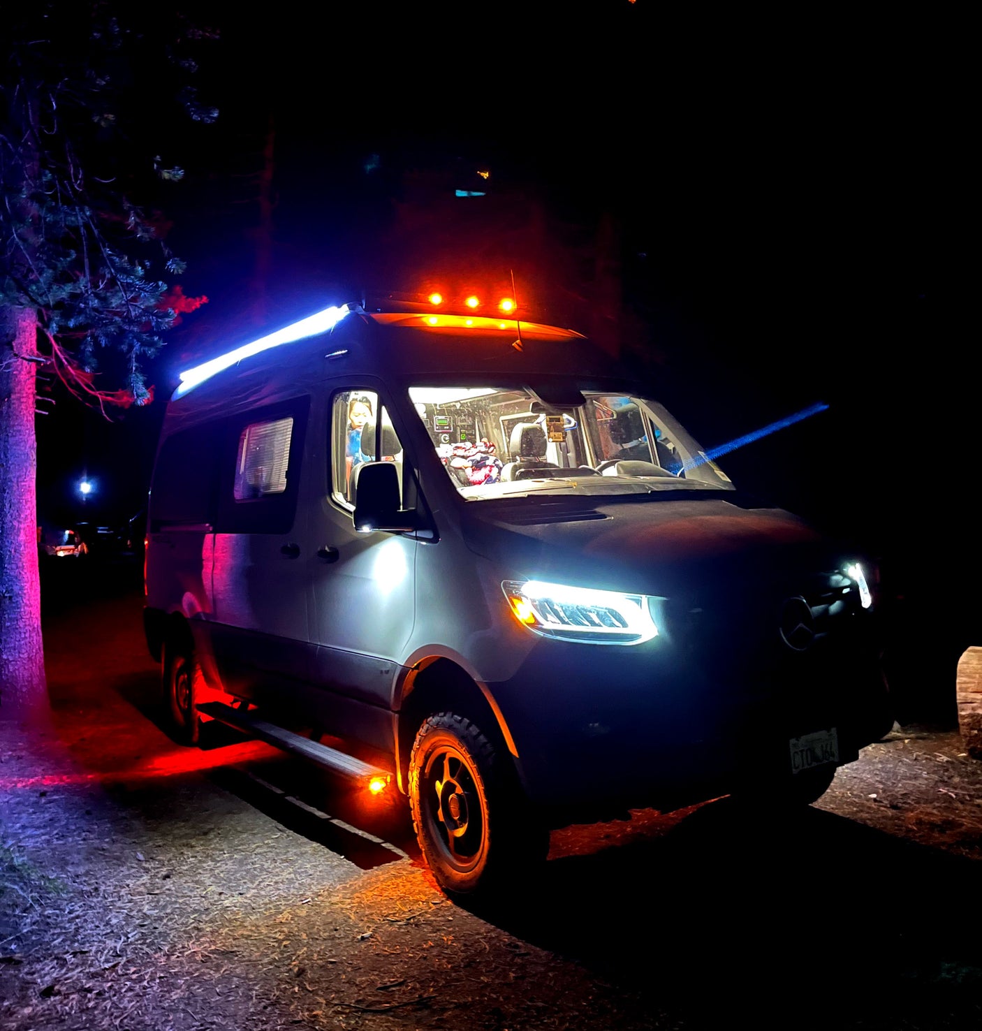 This vibrant RV rental camper van illuminates the night with its colorful lights, parked outdoors under trees.