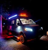 This vibrant RV rental camper van illuminates the night with its colorful lights, parked outdoors under trees.