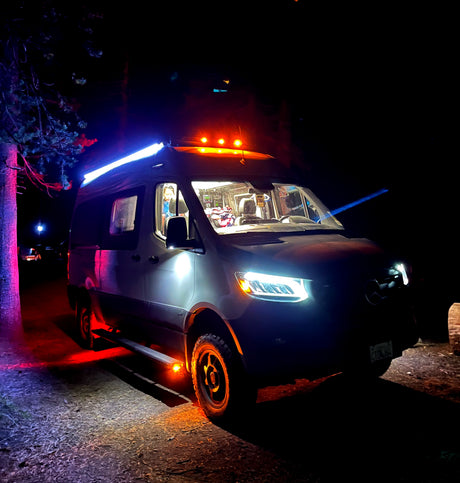 This vibrant RV rental camper van illuminates the night with its colorful lights, parked outdoors under trees.