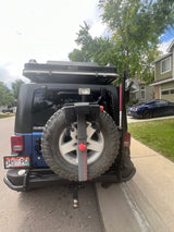Rear view of a blue Jeep Wrangler, featuring a rooftop tent and bike rack, prepared for outdoor adventures. Great for an RV rental trip!