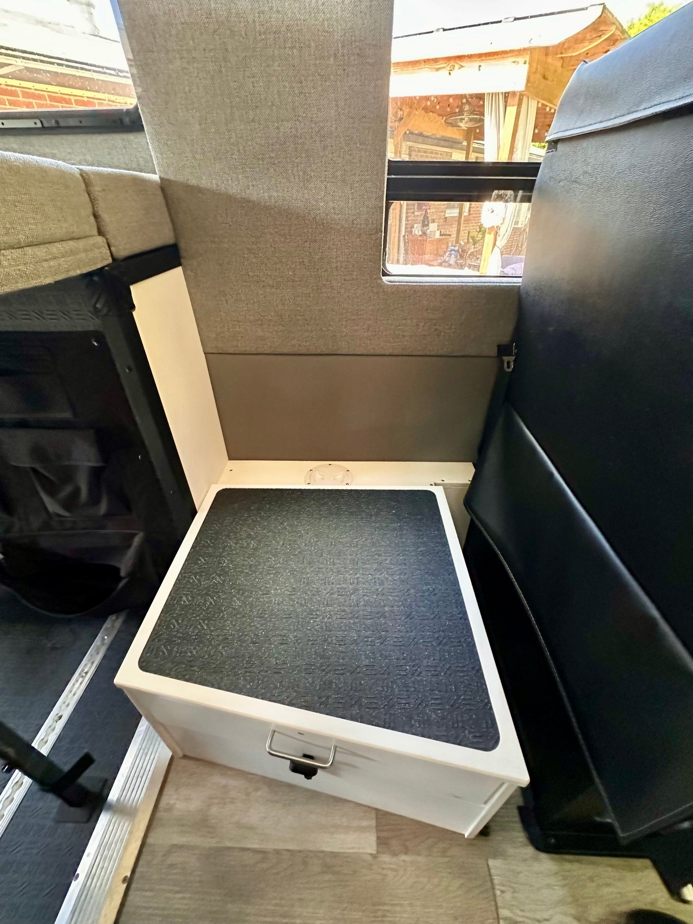RV rental interior with a white step/storage box (with non-slip top) between grey and black seating, by a side window.