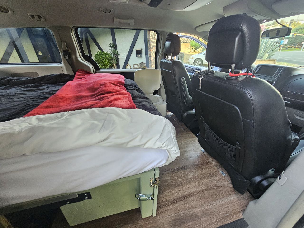 Minivan interior transformed into a camper, with a bed setup, storage, and wood floor. Great RV rental option. — photo 6