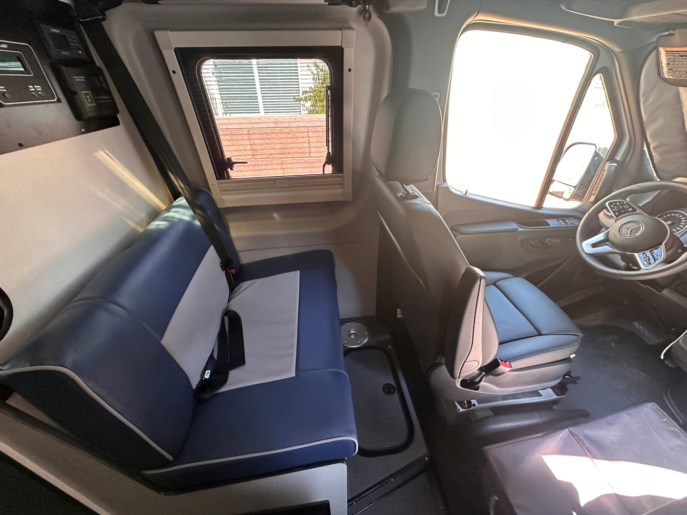 Spacious RV rental interior with bench seating, driver's cockpit, side window, & power management panel.