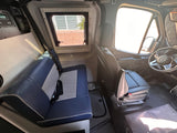 Spacious RV rental interior with bench seating, driver's cockpit, side window, & power management panel.